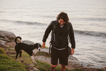 Männlicher Wanderer mit Hund auf einem Felsen am Meer - CAVF31386