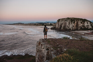 Rear view of male hiker standing on cliff at beach during sunset - CAVF31388