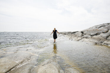 Rückansicht einer im Meer watenden reifen Frau in den Stockholmer Schären - FOLF05731