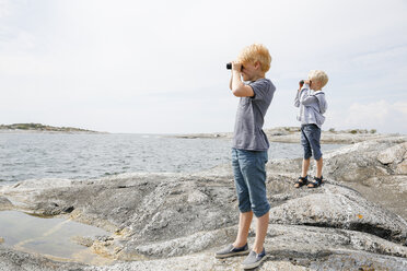 Zwei Jungen schauen durch ein Fernglas am felsigen Meeresufer in den Stockholmer Schären - FOLF05732