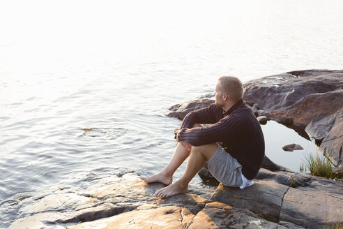 Mature man sitting on rocky lakeshore in the Stockholm archipelago - FOLF05740