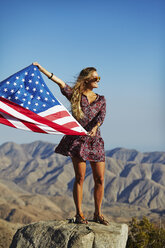 Junge blonde Frau mit US-Flagge vor einer Berglandschaft - FOLF05759