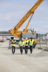 Construction workers walking with crane in background - FOLF05804