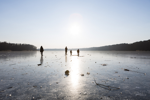 Deutschland, Brandenburg, Straussee, zugefrorener See und Silhouetten von Menschen, die auf dem Eis laufen, lizenzfreies Stockfoto