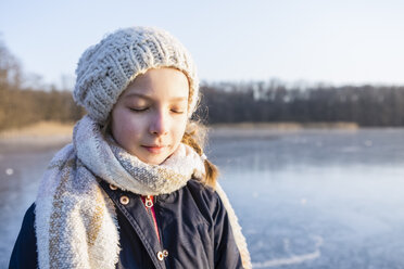 Germany, Brandenburg, Lake Straussee, portrait of a girl standing on frozen lake, eyes closed - OJF00253