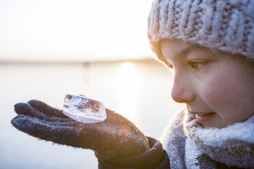 Deutschland, Brandenburg, Straussee, Porträt eines Mädchens, das auf einem zugefrorenen See steht und ein Stück Eis auf seiner Hand betrachtet - OJF00260