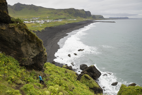 Wanderer schaut von einer Klippe auf einen schwarzen Sandstrand in Island, lizenzfreies Stockfoto
