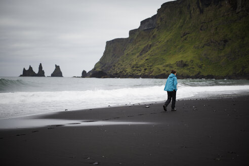 Wanderer am schwarzen Sandstrand am Fuße einer Klippe in Island - FOLF05869