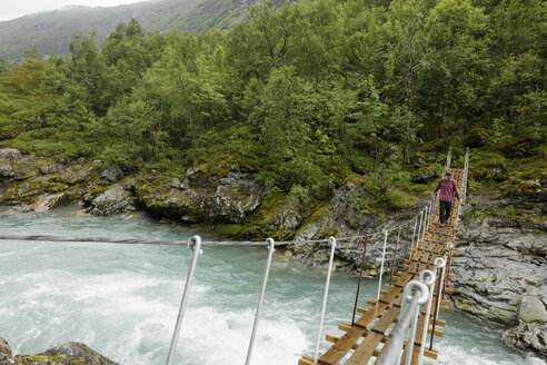 Mann geht auf Hängebrücke über den Fluss in Jotunheimen - FOLF05902