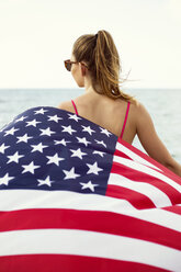 Rückansicht einer jungen Frau mit amerikanischer Flagge am Strand - CAVF31609