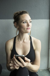 Nachdenkliche Frau mit Smartphone im Fitnessstudio - CAVF31630