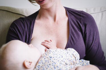 Midsection of mother breastfeeding to daughter while sitting on sofa at home - CAVF31643