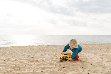 Boy playing with toy truck at beach against cloudy sky - CAVF31648