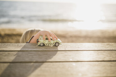 Junge spielt mit Spielzeugauto auf Holzplanke am Strand - CAVF31650