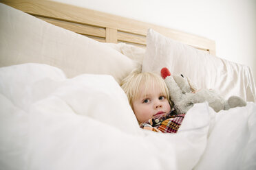 Portrait of cute boy with stuffed toy relaxing on bed at home - CAVF31652