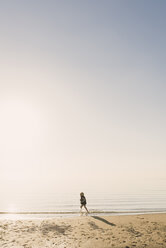 Seitenansicht eines Jungen mit Schwimmweste, der bei nebligem Wetter im Meer läuft - CAVF31664