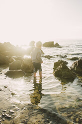 Rear view of boy standing in sea against sky during sunny day - CAVF31665