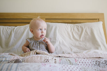 Baby-Mädchen schaut weg, während sie auf dem Bett zu Hause sitzt - CAVF31668