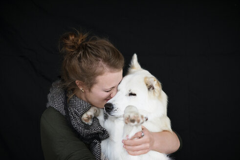 Happy woman holding dog against black background - CAVF31697