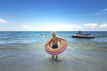 Rear view of boy carrying inner tube while walking towards sea - CAVF31704