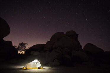 Illuminated tent by rock formation against starry sky - CAVF31709