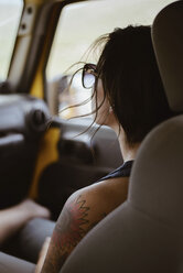 Junge Frau mit Tätowierung auf der Schulter sitzt in einem Geländewagen - CAVF31724