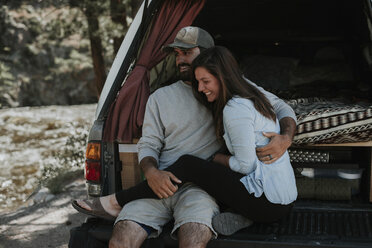 Happy young couple sitting in car trunk - CAVF31743