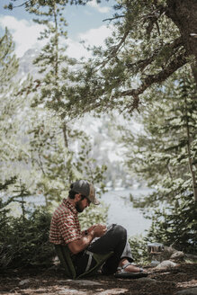 Side view of hiker sitting in camping seat at forest - CAVF31757