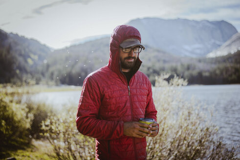 Wanderer mit Kapuze, der eine Getränkedose hält, während er am See im Grand Teton National Park steht - CAVF31759