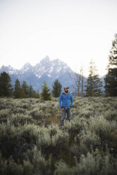 Wanderer mit den Händen in den Taschen steht auf einem Feld vor den Bergen und dem klaren Himmel im Grand Teton National Park - CAVF31761