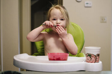 Portrait of girl eating food while sitting on high chair at home - CAVF31830