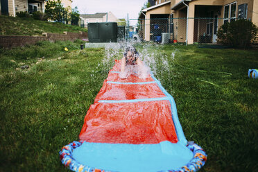 Girl enjoying on water slide in lawn - CAVF31841