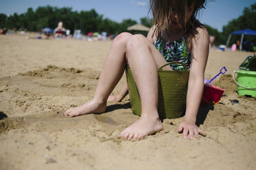 Mädchen sitzt im Eimer am Strand - CAVF31846