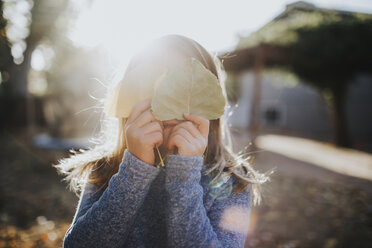 Girl hiding face with leaves on sunny day - CAVF31867