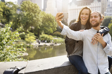 Happy couple taking selfie while leaning on retaining wall - CAVF31878