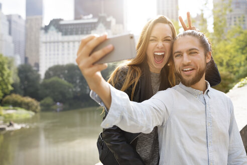 Fröhliches Paar, das ein Selfie macht, während es sich auf eine Stützmauer stützt - CAVF31879