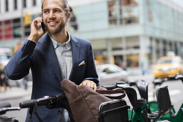 Businessman talking on mobile phone while standing at parking lot in city - CAVF31889