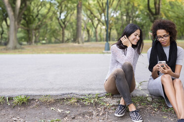 Friends using mobile phone while sitting on footpath in park - CAVF31909