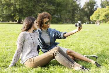 Freunde fotografieren auf einer Wiese im Park sitzend - CAVF31919