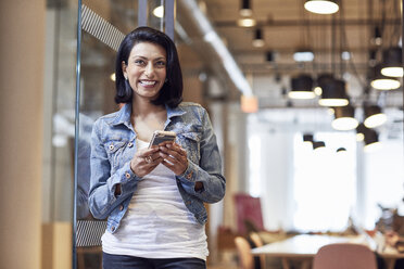 Happy businesswoman looking away while holding smart phone in office - CAVF32007