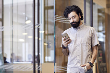 Geschäftsmann, der ein Smartphone benutzt, während er an der Tür im Büro steht - CAVF32009