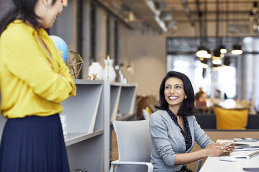 Happy businesswoman looking at female colleague while sitting in creative office - CAVF32024