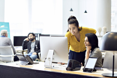 Geschäftsfrauen arbeiten an einem Desktop-Computer, im Hintergrund sitzen männliche Kollegen - CAVF32025