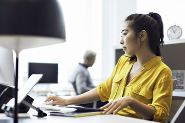 Geschäftsfrau arbeitet an einem Desktop-Computer, im Hintergrund sitzt ein männlicher Kollege - CAVF32027