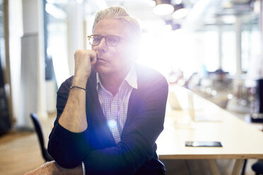 Portrait of confident senior businessman sitting in brightly lit creative office - CAVF32053