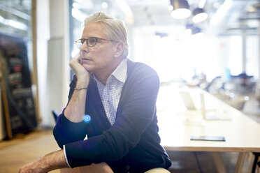 Thoughtful senior businessman looking away while sitting in brightly lit office - CAVF32055