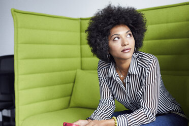 Businesswoman looking away while sitting on sofa in office - CAVF32069