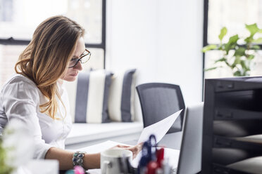 Seriöse Geschäftsfrau studiert Dokumente im Büro - CAVF32094