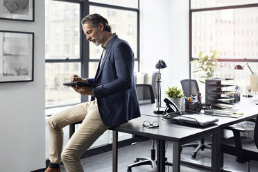 Geschäftsmann, der einen Tablet-Computer benutzt, während er auf einem Schreibtisch im Büro sitzt - CAVF32098