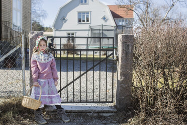 Als Osterhexe verkleidetes Mädchen mit Osterkorb am Tor stehend - FOLF05936